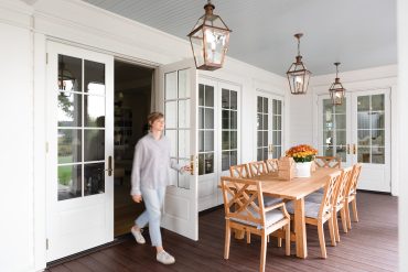 Image of a woman walking through French doors onto a deck with a dining table